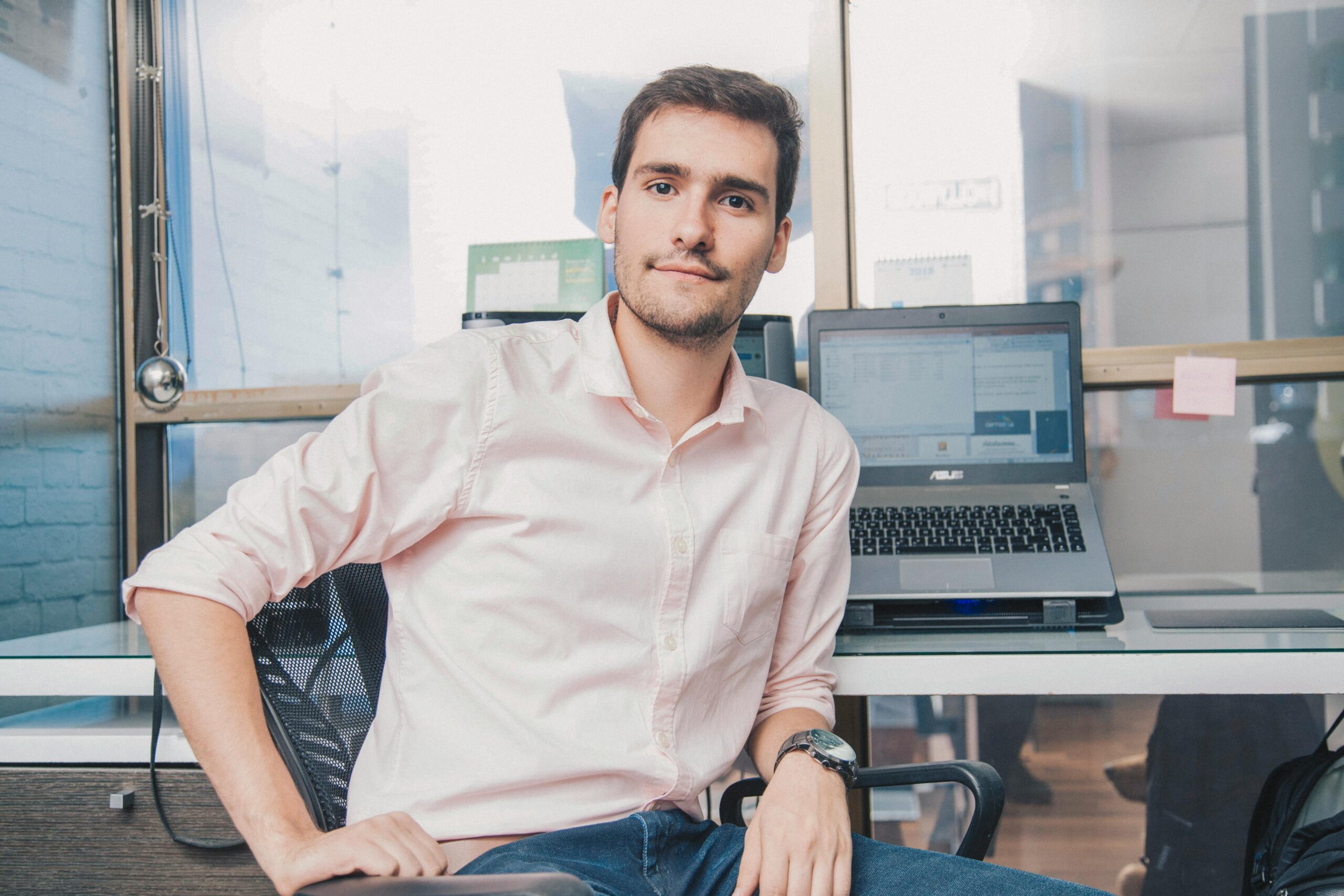 Confident young man in shirt working in modern office with laptop and desk accessories.